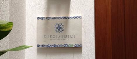 A sign with the text "DIECISEDICI YOUR HOME IN AMALFI" on a white wall.