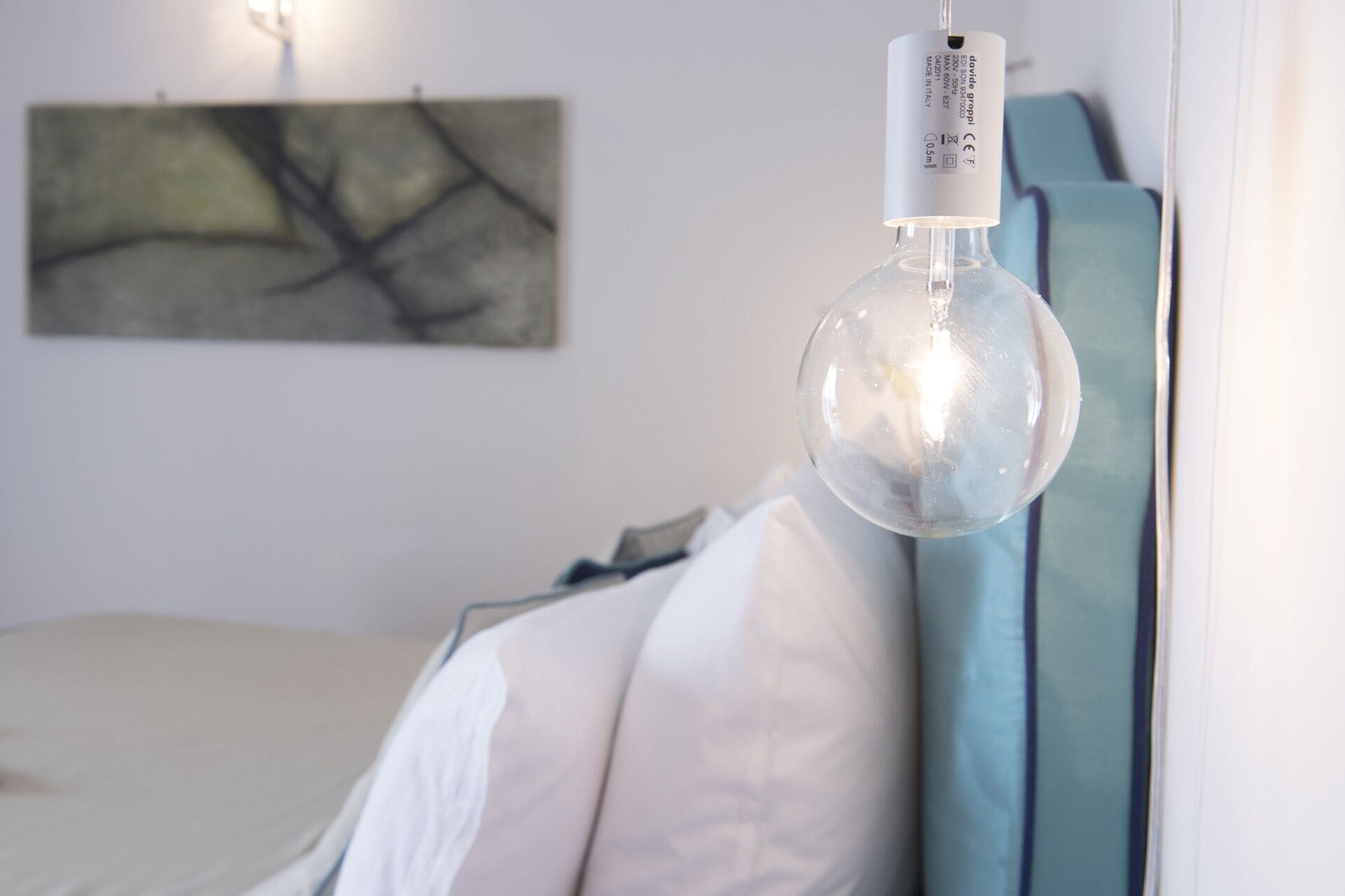 A modern bedroom with a bed, a wall-mounted light fixture, and a piece of abstract art.