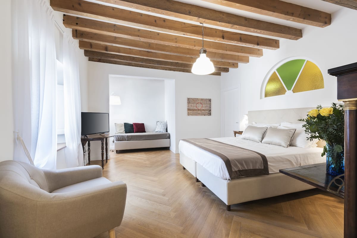A bedroom with a bed, a sofa, a TV, and a dining table.