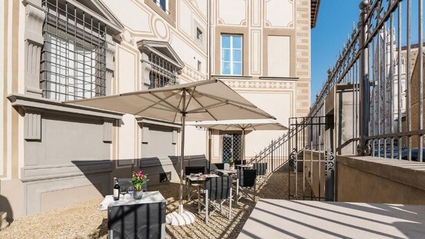 An outdoor seating area with tables and umbrellas, a building with classical architecture, and a staircase.