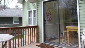 A green house with a wooden deck, a sliding glass door, and a small table.