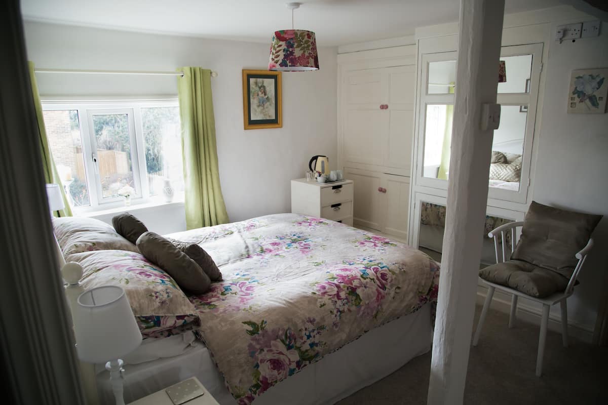 A bedroom with a bed, bedside table, chair, and a window with curtains.
