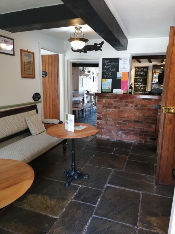 A cozy interior with a stone floor, wooden furniture, and a chalkboard with event information.