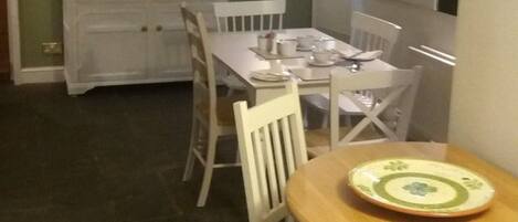 Un comedor con una mesa dispuesta para cuatro personas, sillas blancas y un armario blanco con vajilla.