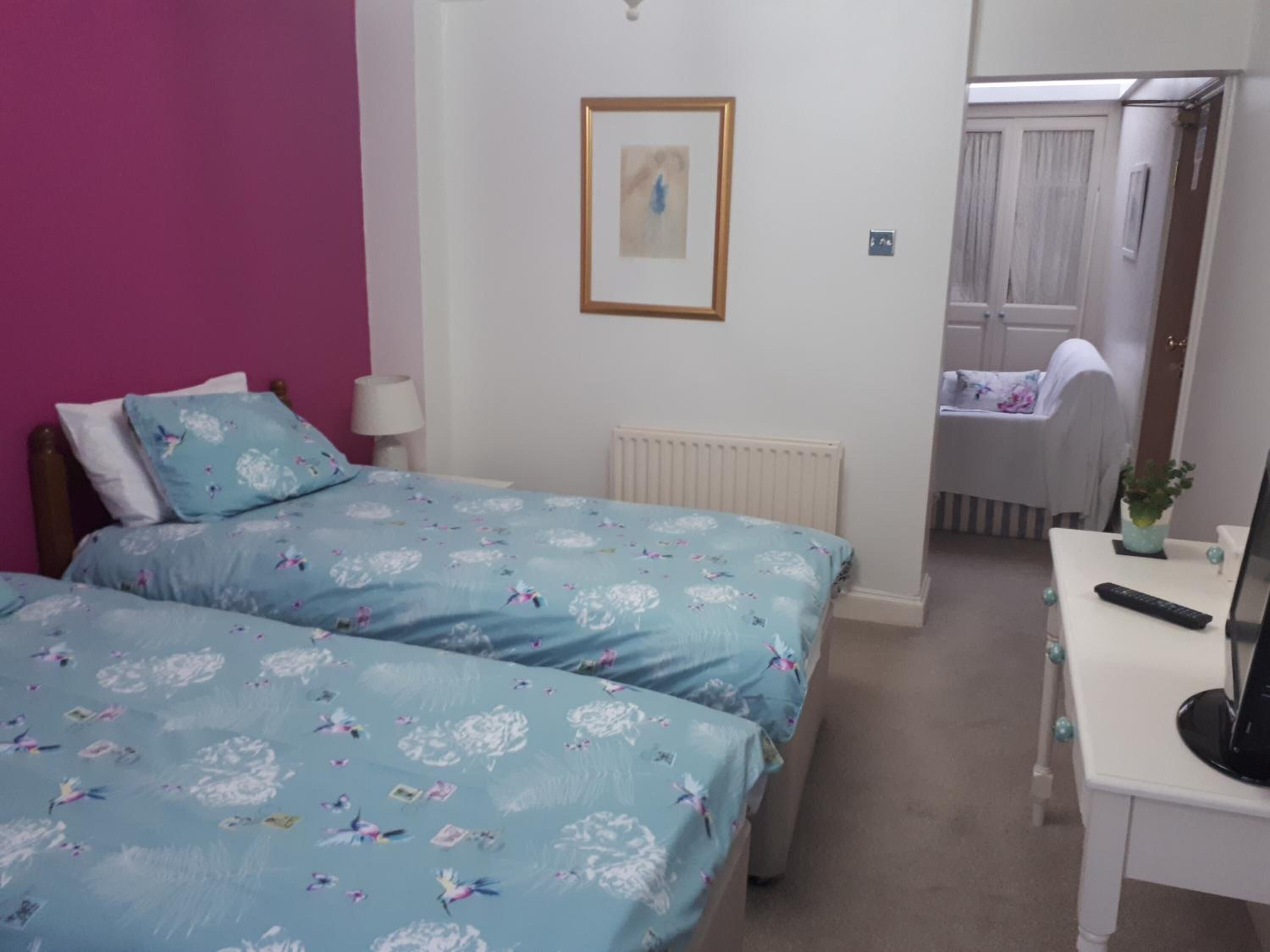 Een slaapkamer met twee bedden, een bureau, een radiator en een deur naar een badkamer.