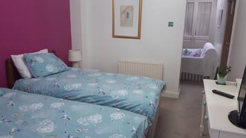 Een slaapkamer met twee bedden, een bureau, een radiator en een deur naar een badkamer.