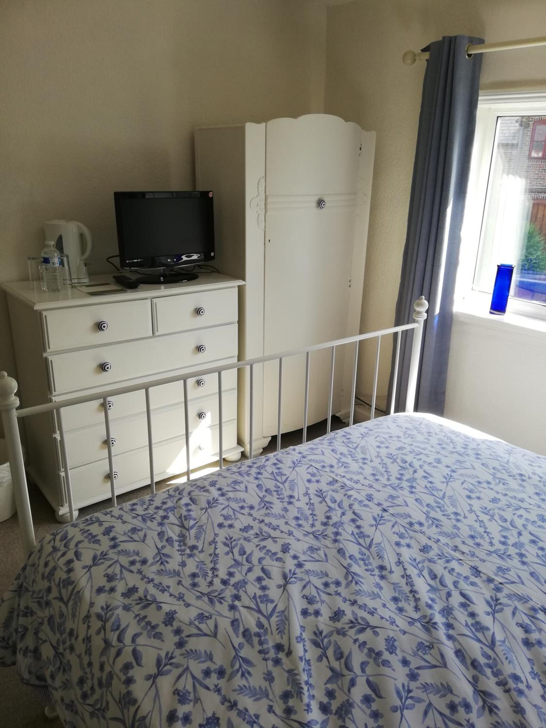 A bedroom with a bed, a dresser, a television, and a window with curtains.