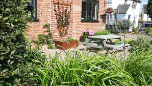 Une maison en briques avec un jardin, une tonnelle en bois et un banc.