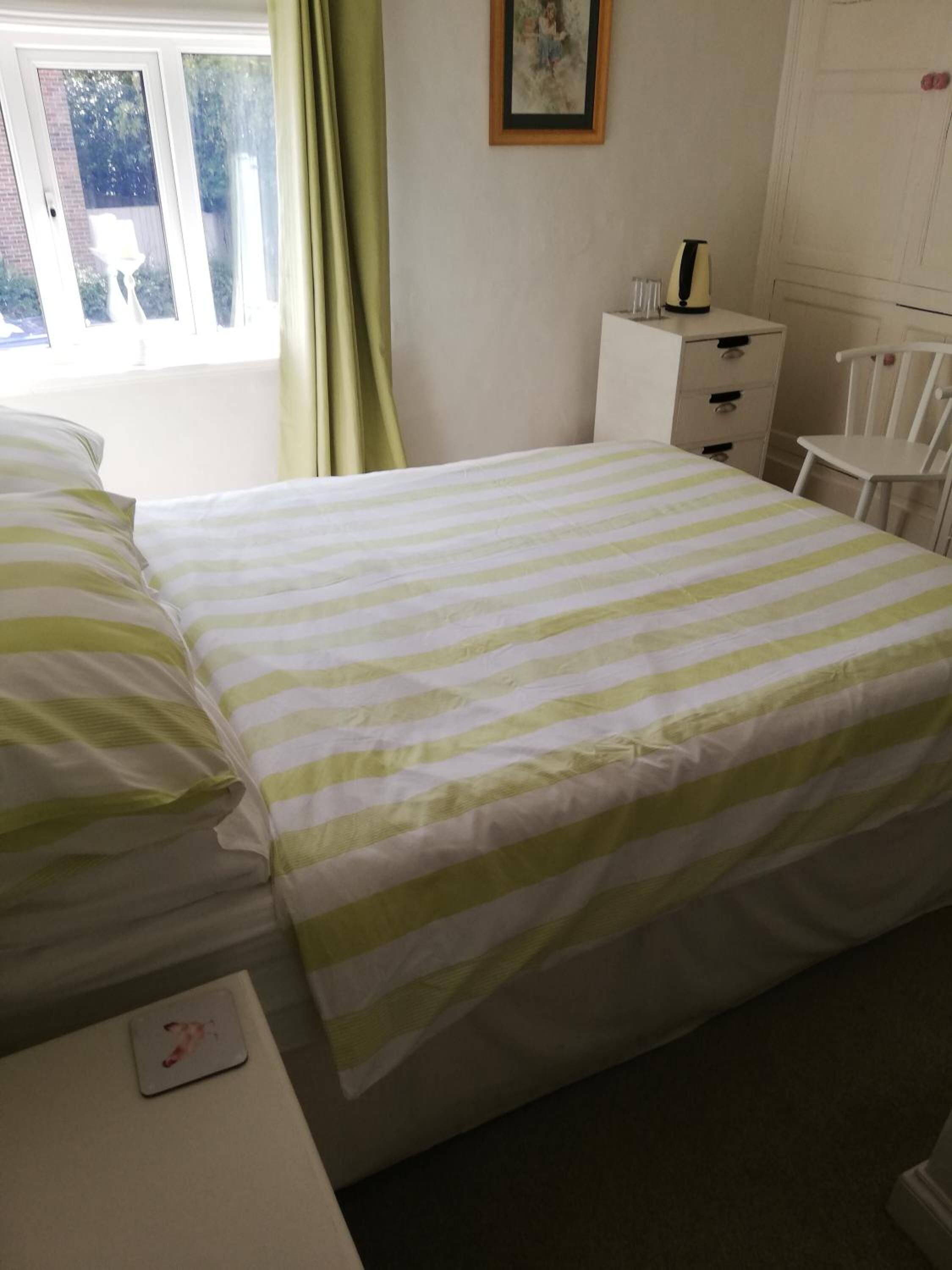 A bedroom with a bed, a nightstand, a chair, a dresser, and a window with curtains.