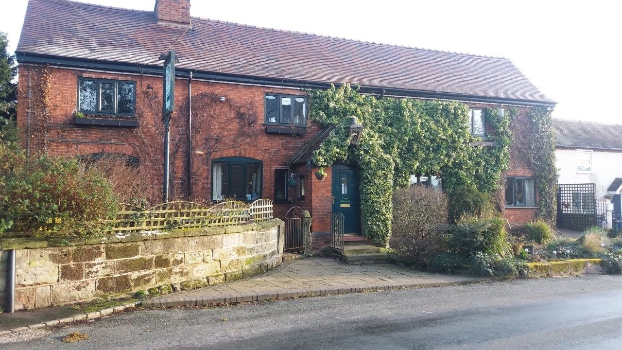 A two-story brick house with a green door and windows, a stone wall, and a paved driveway.