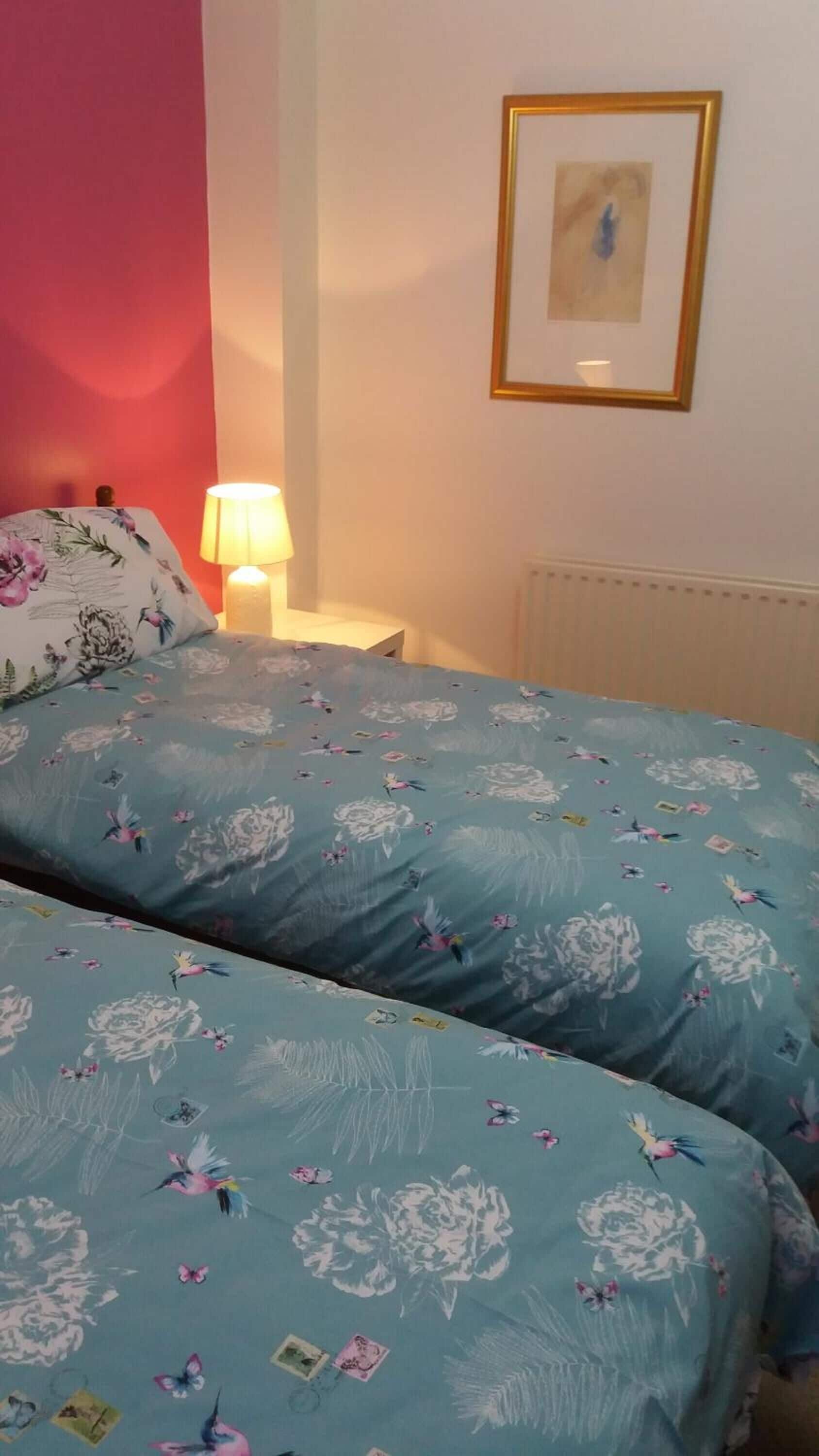 A bedroom with two beds, a nightstand, a lamp, and a framed picture on the wall.