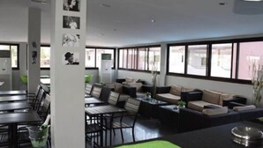 A modern indoor space with a mix of seating arrangements, including tables and sofas, and large windows providing natural light. - Hotel Moatize (Moatize)