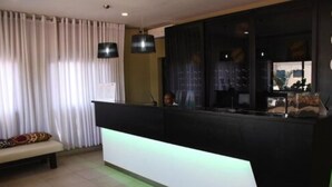 A modern reception area with a black counter, a bench with a patterned cushion, and a large window with curtains. - Hotel Moatize (Moatize)