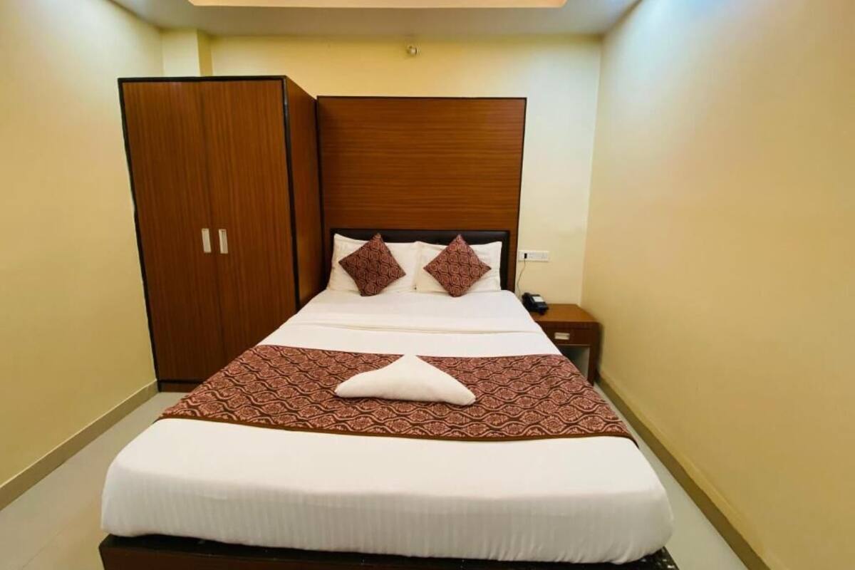 A neatly made bed with a patterned bedspread, a wooden headboard, and a wardrobe to the left.