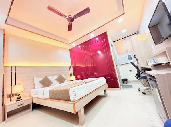 A modern bedroom with a bed, bedside tables, a ceiling fan, a red door, and a TV. - Kamat Inn (Patna)