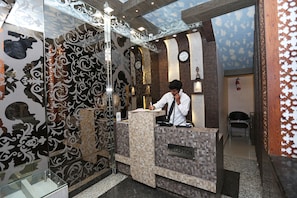 A reception desk with a 'RECEPTION' sign, ornate wall patterns, and a clock. - Kamat Inn (Patna)