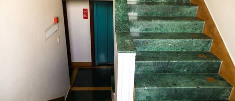 A staircase with green marble steps and a white handrail, leading to a door with a red emergency exit sign.