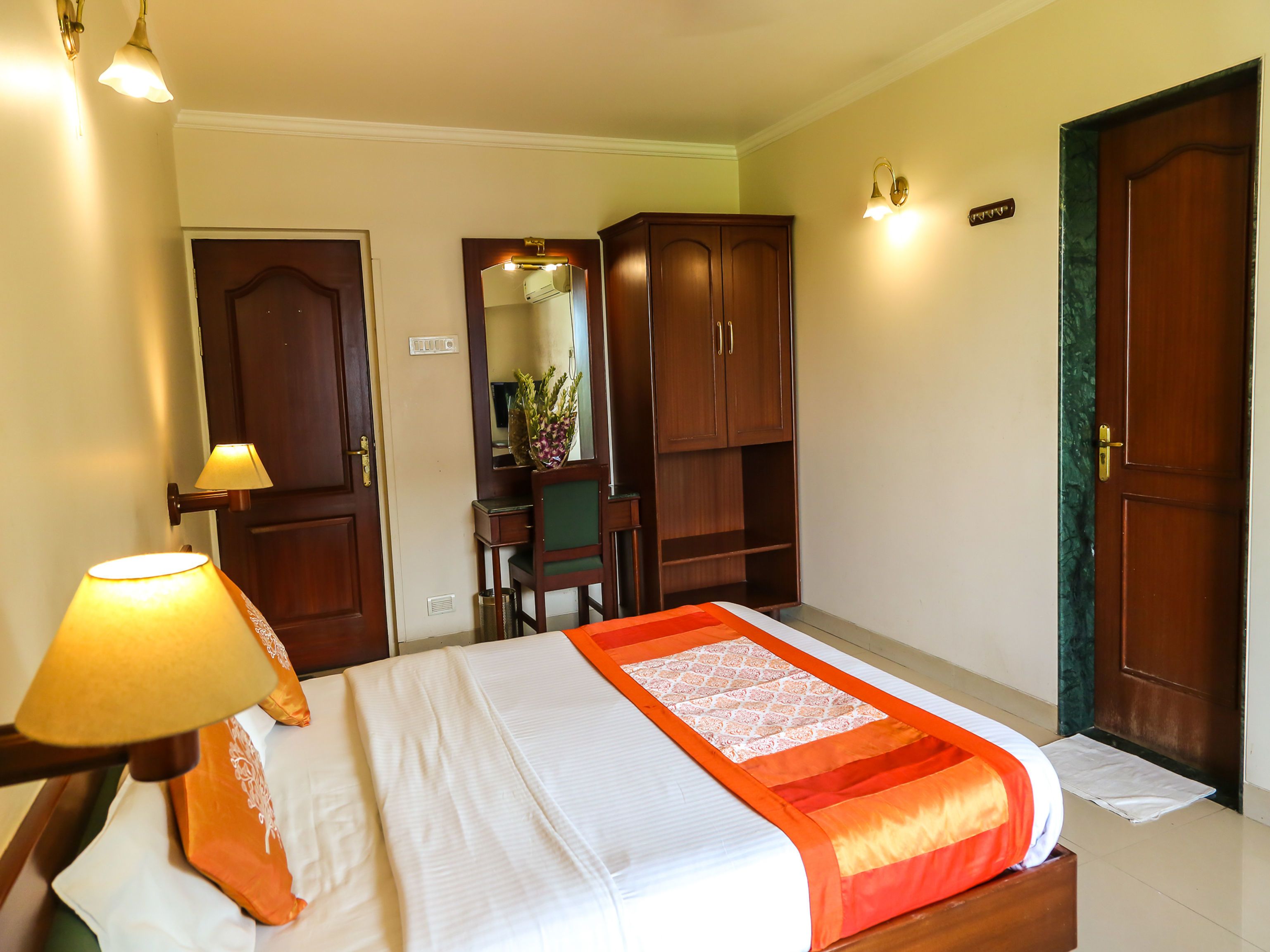 A hotel room with a bed, a desk with a chair, a mirror, and a wardrobe.