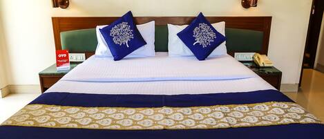 A hotel room with a neatly made bed, two nightstands with lamps, a telephone, and a sign on the nightstand.