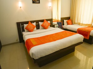 Een hotelkamer met twee bedden, elk voorzien van wit beddengoed en oranje accenten, een nachtkastje met een lamp, en een spiegel aan de muur.