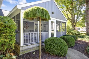 Une maison avec un porche abrité, un petit jardin avec des arbustes soigneusement taillés et un arbre taillé en forme décorative.