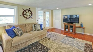 Sala de estar con sofá color beige, alfombra estampada, mueble de televisión de madera y un adorno de timón.