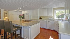 Una cocina con gabinetes blancos, encimera de granito, estufa integrada, lavavajillas y una ventana que proporciona luz natural.
