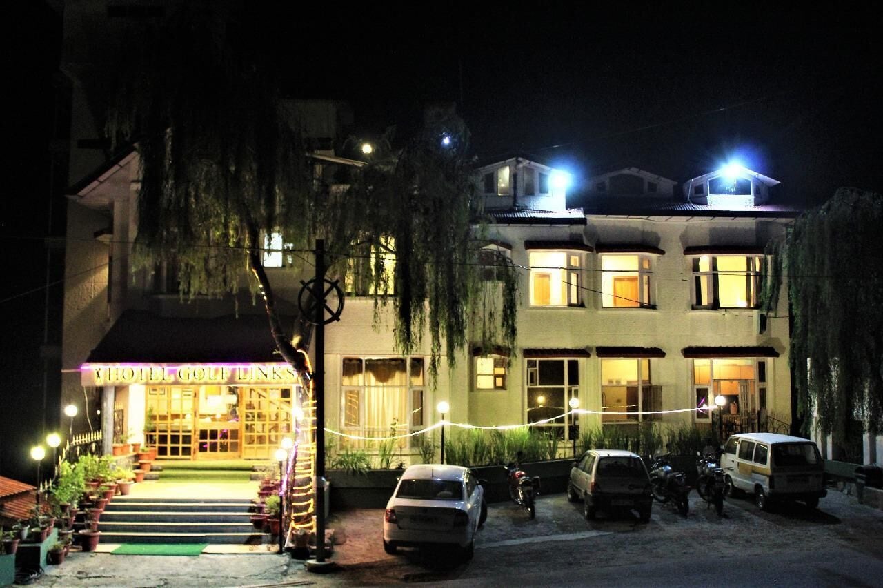 A hotel with a well-lit entrance, a visible staircase leading to the entrance, and several parked vehicles in the parking area.