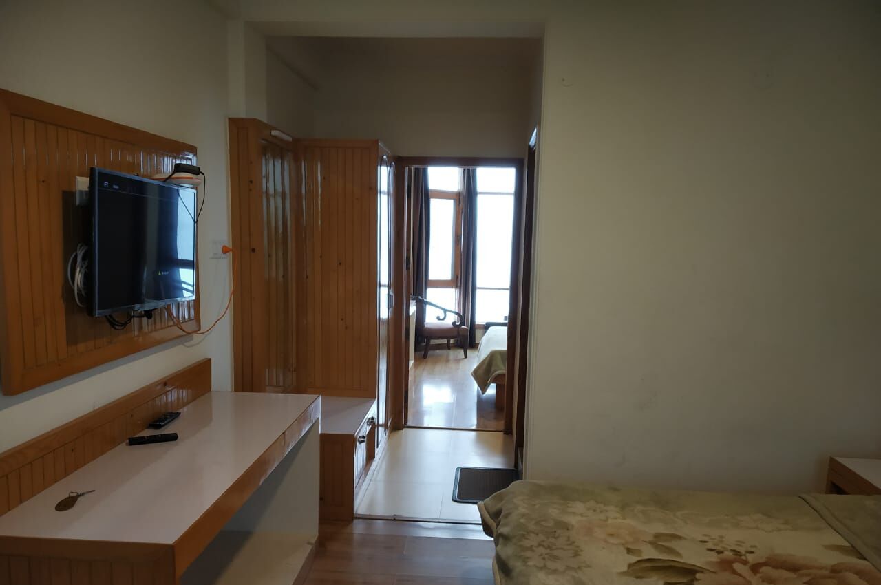 A room with a wooden bench, a television mounted on the wall, and a bed with a patterned bedspread.