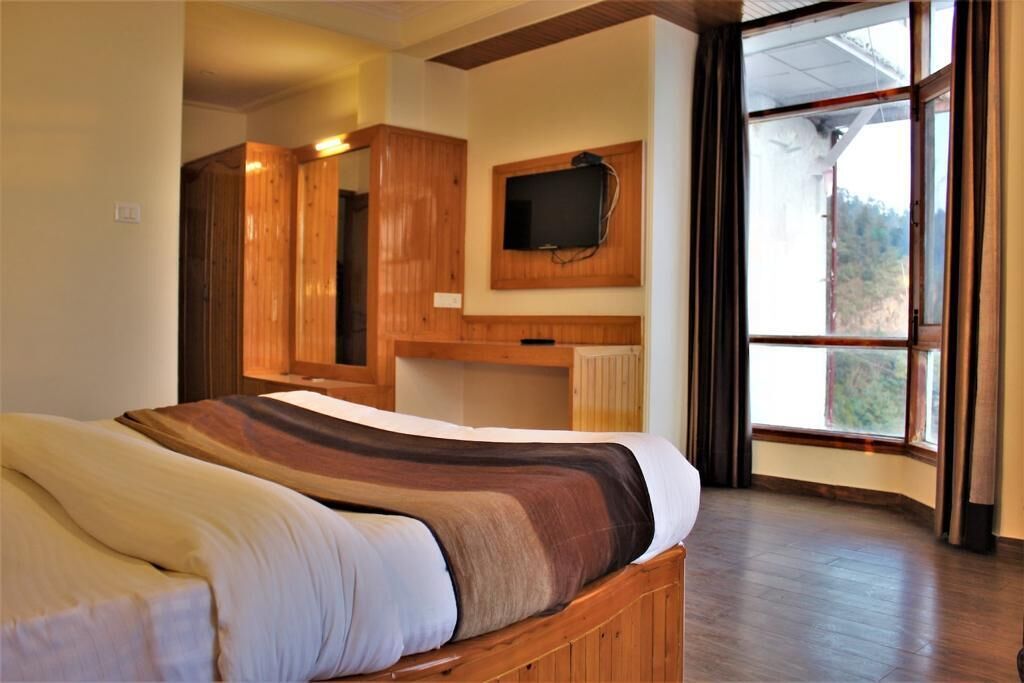 A bedroom with a wooden bed, a television mounted on the wall, and a large window with curtains.