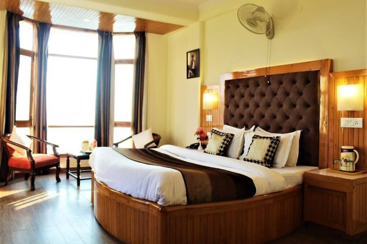 Ein Hotelzimmer mit einem großen Bett, einem hölzernen Kopfteil, einem Schreibtisch, einem Stuhl und einem Fenster mit Vorhängen.