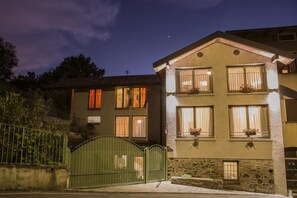 Kaksikerroksinen rakennus, jossa on useita ikkunoita, joista osassa on verhot, ja etualalla näkyy vihreä portti.