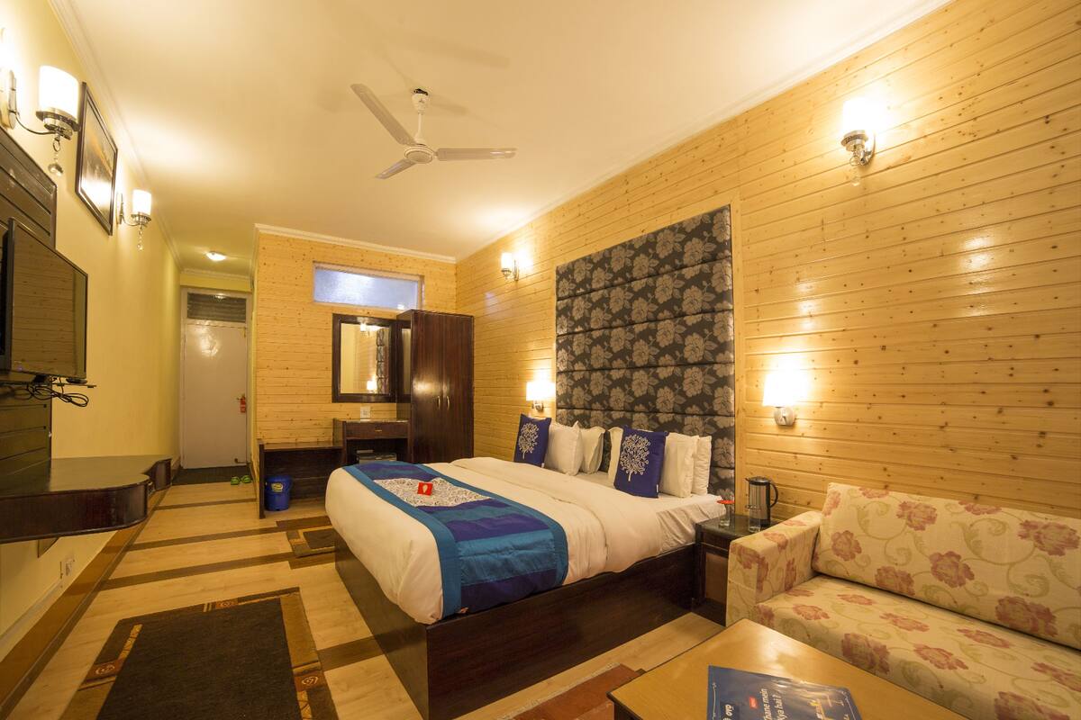 A hotel room with a bed, a sofa, a desk, a mirror, and a ceiling fan.
