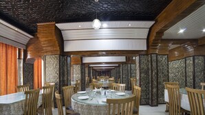 Un restaurante con mesas redondas y sillas de madera, con un muro con motivos y una pared de ladrillo.