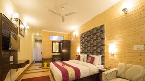 Habitación de hotel con cama, sofá, cabecero de madera, televisor y escritorio con un libro.