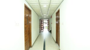 A hallway with wooden doors on both sides, a tiled floor with a black stripe, and a ceiling with a decorative pattern. - OYO 5344 Hotel Oasis (Thiruvananthapuram)