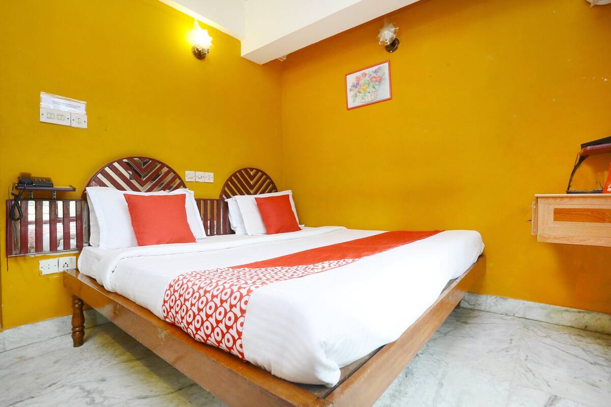 Une chambre d’hôtel équipée d’un lit, d’une table de chevet, d’une prise électrique et d’un luminaire fixé au mur.