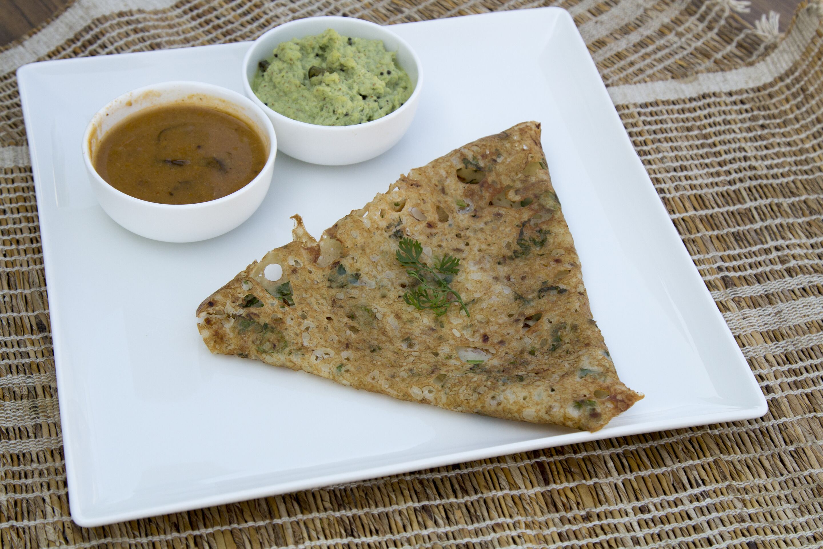 A triangular flatbread on a white plate with two small bowls of dips.