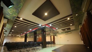 A conference room with rows of chairs, a stage, and a ceiling with red lighting accents. - Hotel Vrundavan Residency (Vadodara)