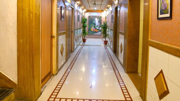 A hotel corridor with a polished floor, wooden doors, and a central plant. - Hotel Vrundavan Residency (Vadodara)