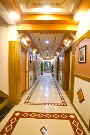 Un couloir d’hôtel avec un sol ciré, des portes en bois et une plante placée au centre.