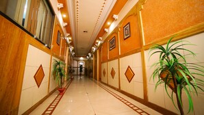 A hotel corridor with tiled floors, decorative wall panels, and potted plants. - Hotel Vrundavan Residency (Vadodara)
