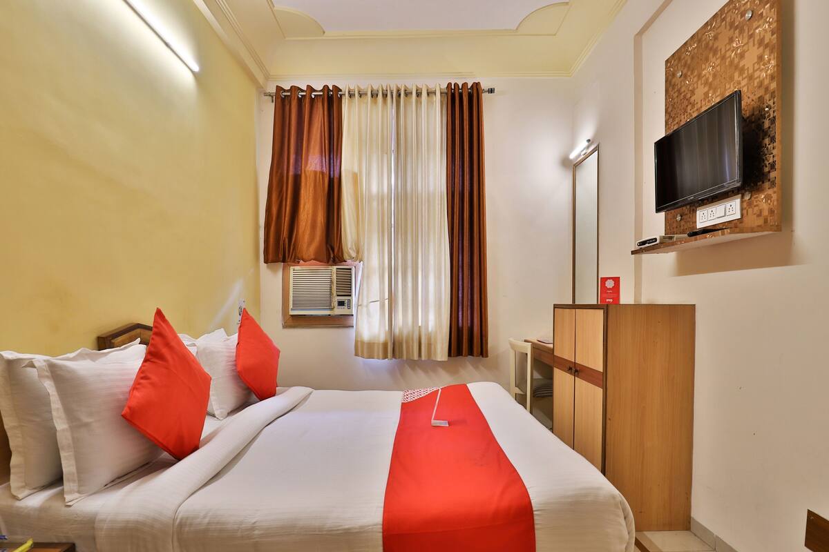 Une chambre d’hôtel équipée d’un lit, d’oreillers, d’un téléviseur fixé au mur, d’un appareil de climatisation et d’une armoire en bois.