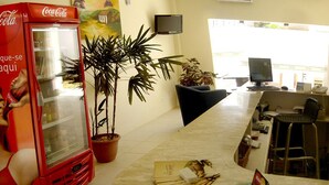 A hallway with a Coca-Cola refrigerator, potted plants, a computer desk, and a chair. - Hotel Portal dos Ventos (Parnaíba)