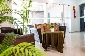 Un moderno vestíbulo de hotel con una zona de estar que incluye un sofá, sillones, una mesa pequeña con una planta y un extintor en la pared.