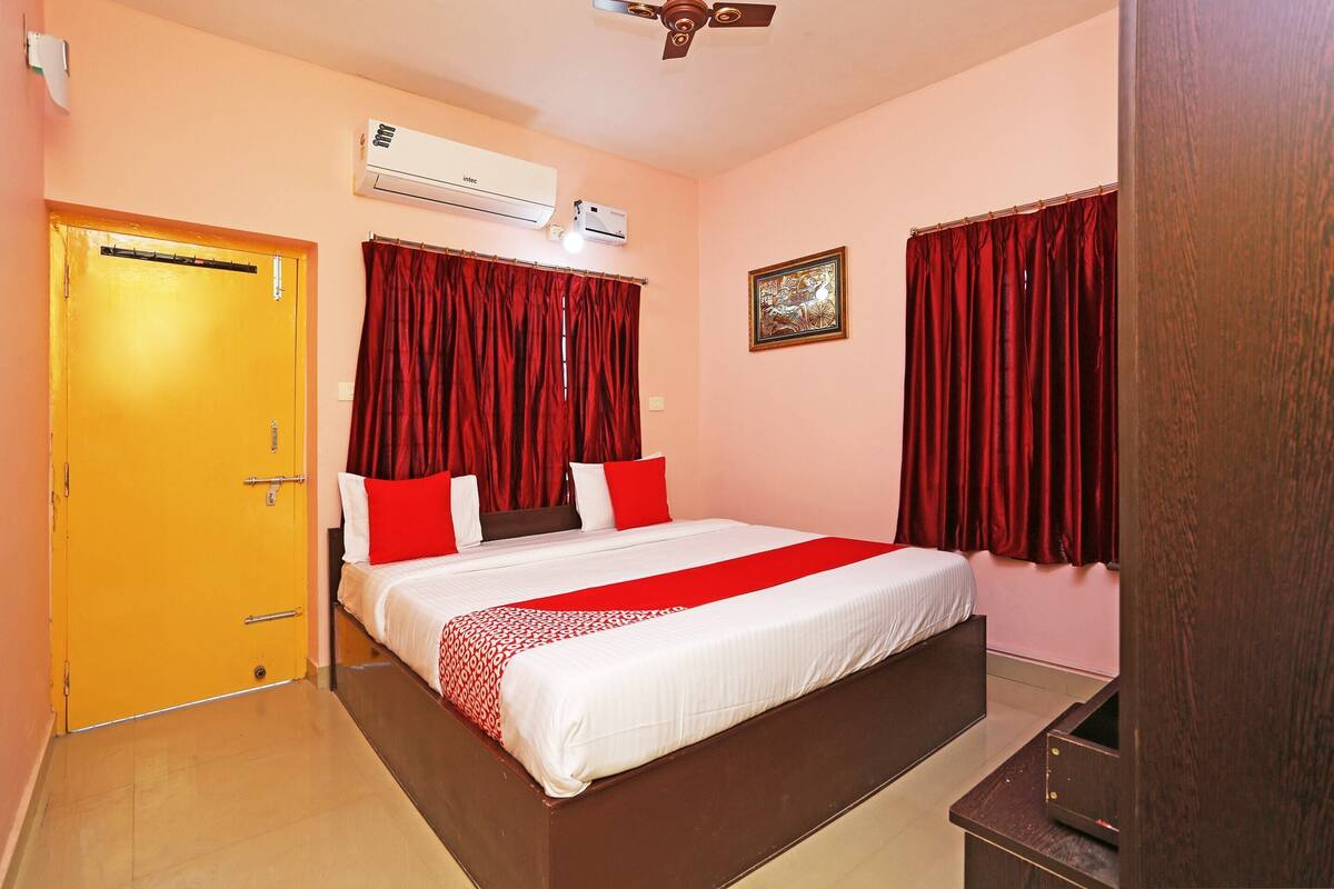 A hotel room with a bed, red curtains, a ceiling fan, and an air conditioning unit.