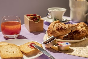Una mesa con un croissant, una taza de té y un pequeño frasco de mermelada.