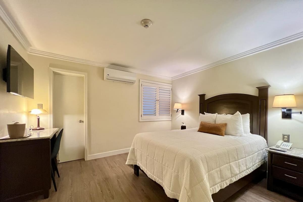 A hotel room with a bed, bedside table, lamp, desk, chair, and a television mounted on the wall.
