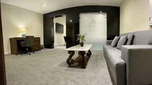 A modern living room with a grey sofa, a wooden coffee table, a desk with a lamp, and a potted plant. - Hotel Caesar's (Tijuana)
