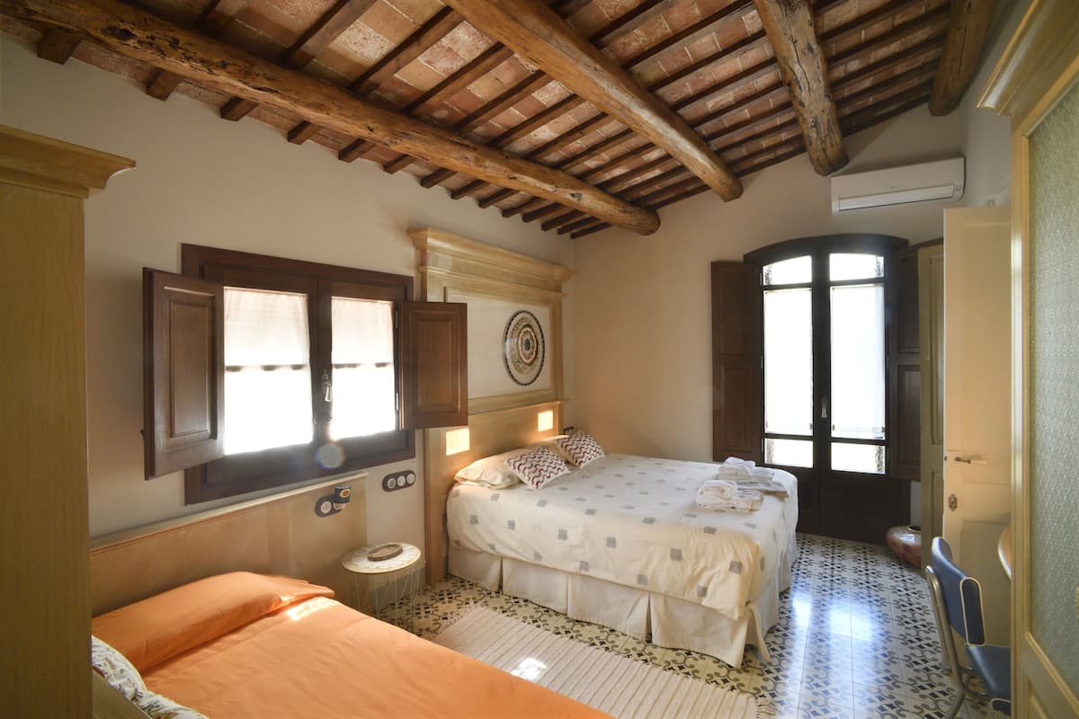 Une chambre à coucher avec un lit, un petit lit, une fenêtre, une porte et un plafond avec des poutres en bois.